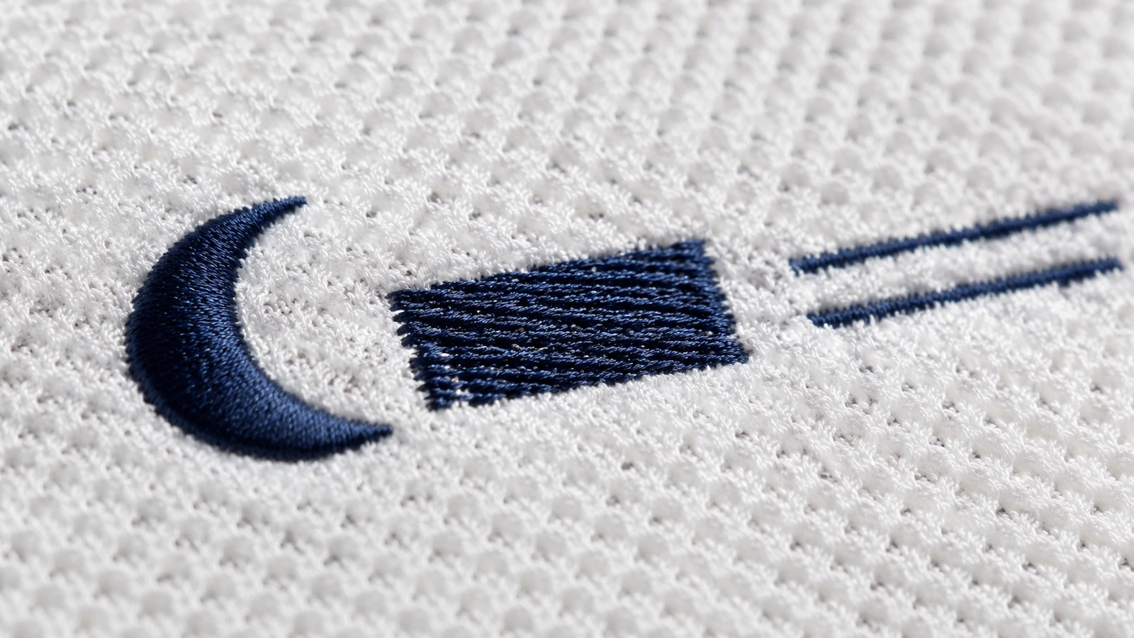 Vista macro di una maglia piqué di cotone con una forma a punto raso liscia, un'area di riempimento con trama in rilievo e sottili linee a punto filza che affondano nelle celle del tessuto