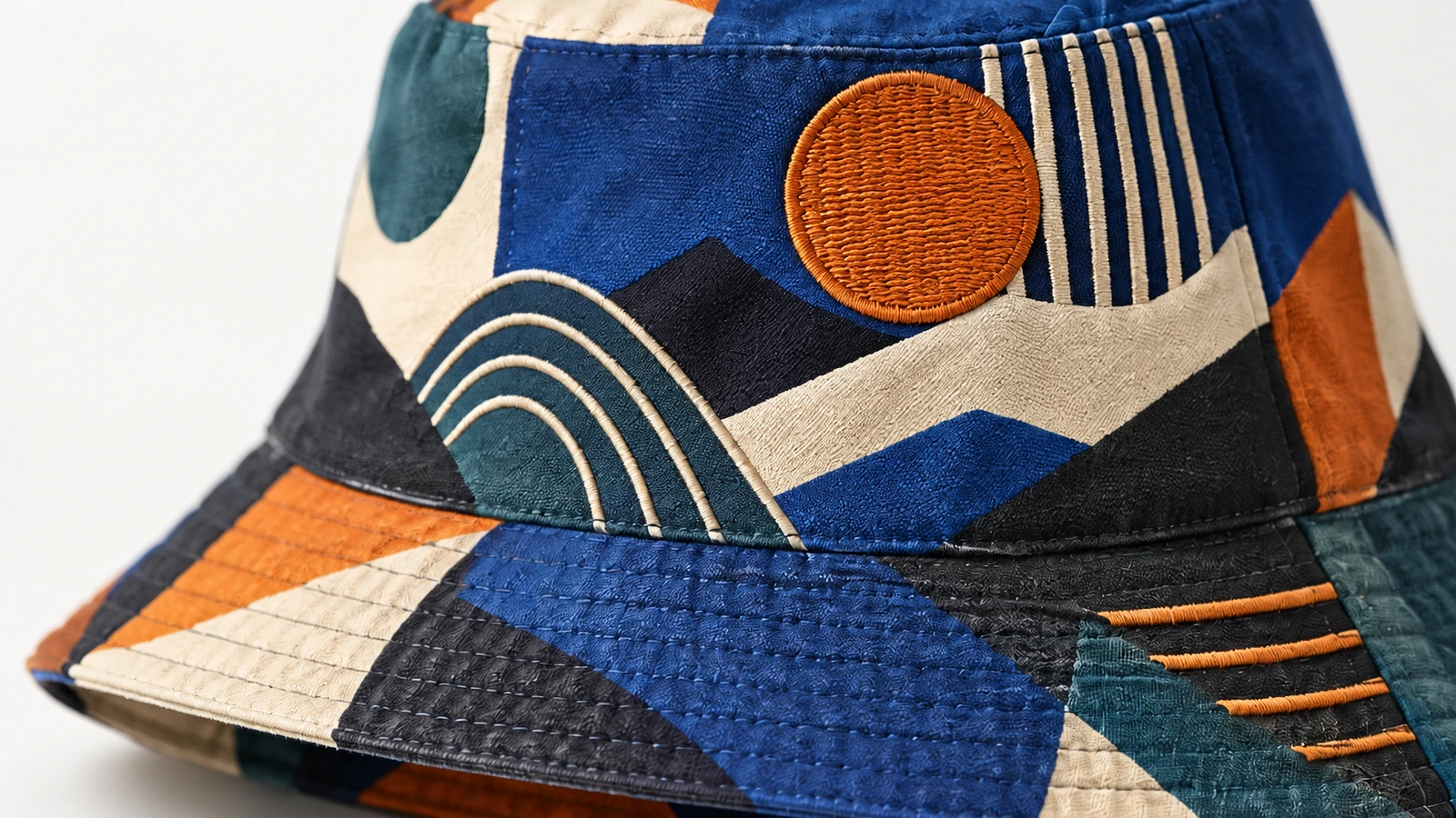 Dettaglio del tessuto e del ricamo della bucket hat Primo piano del tessuto a motivi di una bucket hat, della tesa cucita e del ricamo circolare arancione
