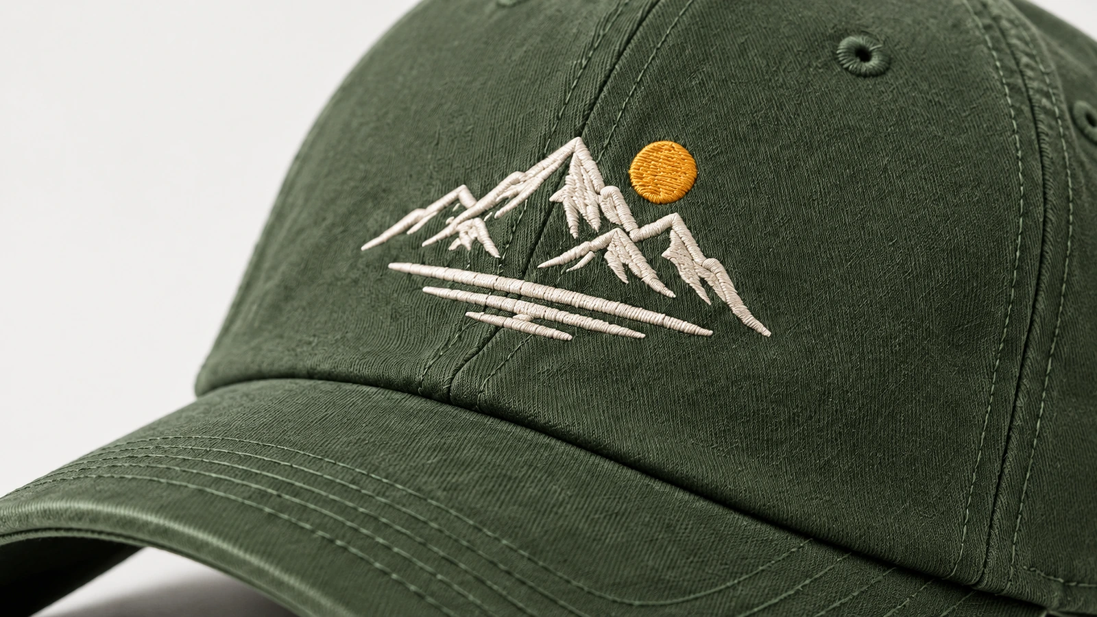 Primo piano di un ricamo bianco a forma di montagna e di un sole giallo su un cappellino verde
