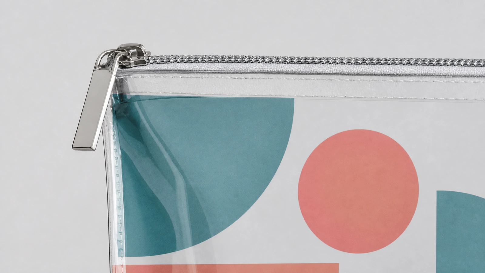 Dettaglio della cerniera e dell'angolo della pochette Primo piano di un cursore della cerniera color argento e dell'angolo di una pochette trasparente stampata