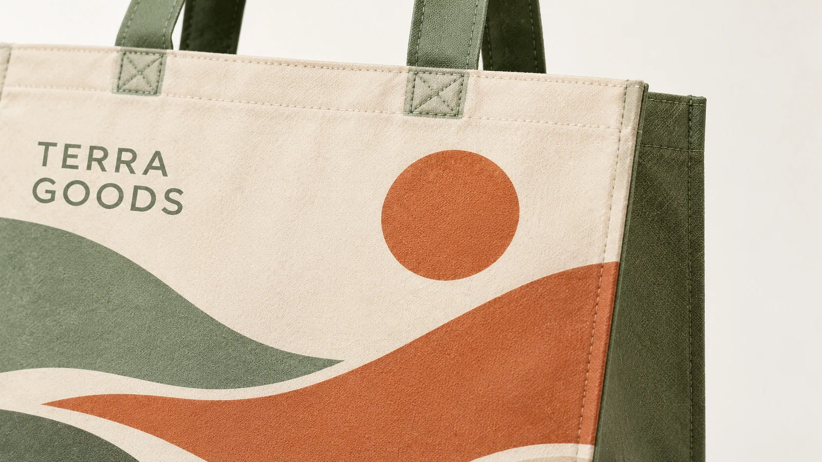 Primo piano di una tote con stampa paesaggio, scritta TERRA GOODS e manici verdi cuciti