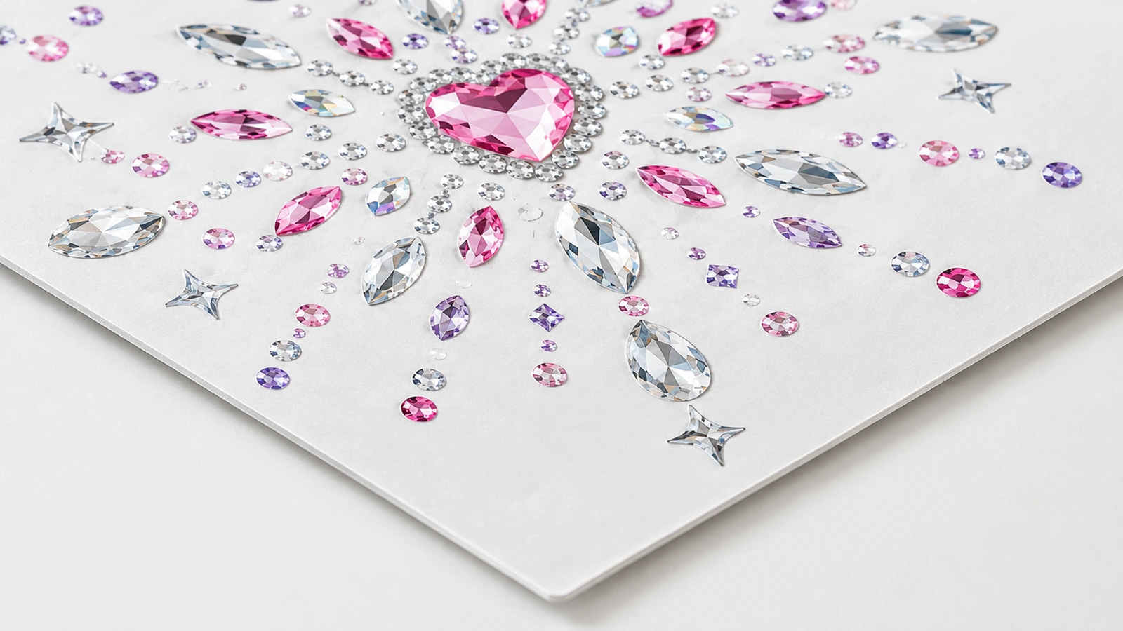 Primo piano di un motivo di strass rosa con centro a cuore e strass trasparenti, rosa e viola, su un foglio bianco