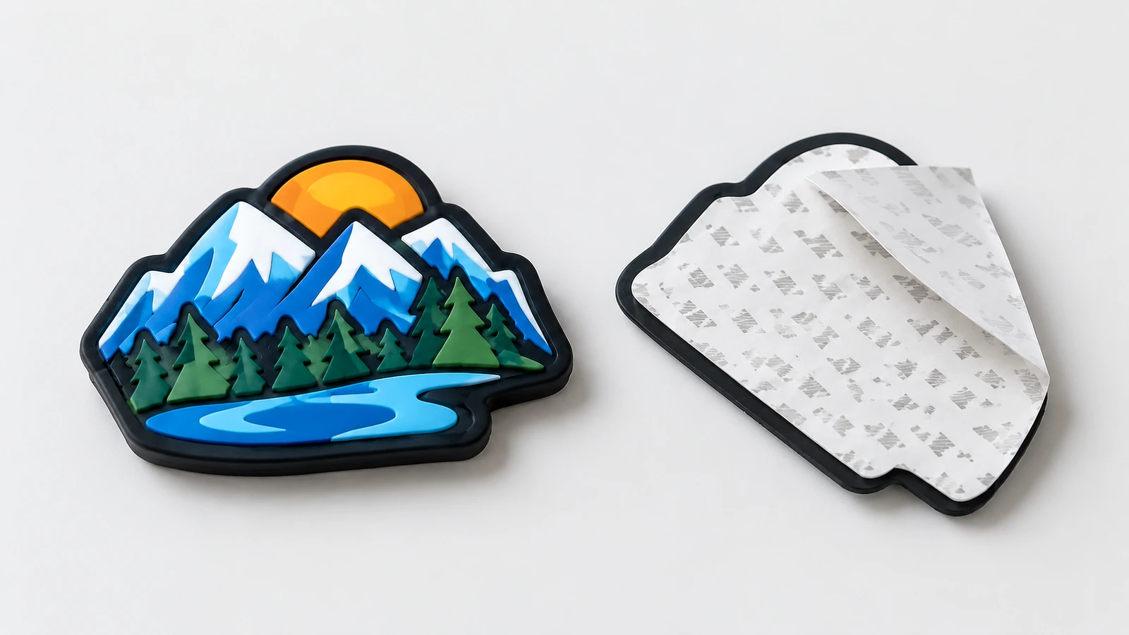 Fronte dell'etichetta in rilievo e retro adesivo Etichetta in PVC morbido con grafica di montagna, mostrata a faccia in su accanto al retro adesivo e al supporto siliconato parzialmente staccato