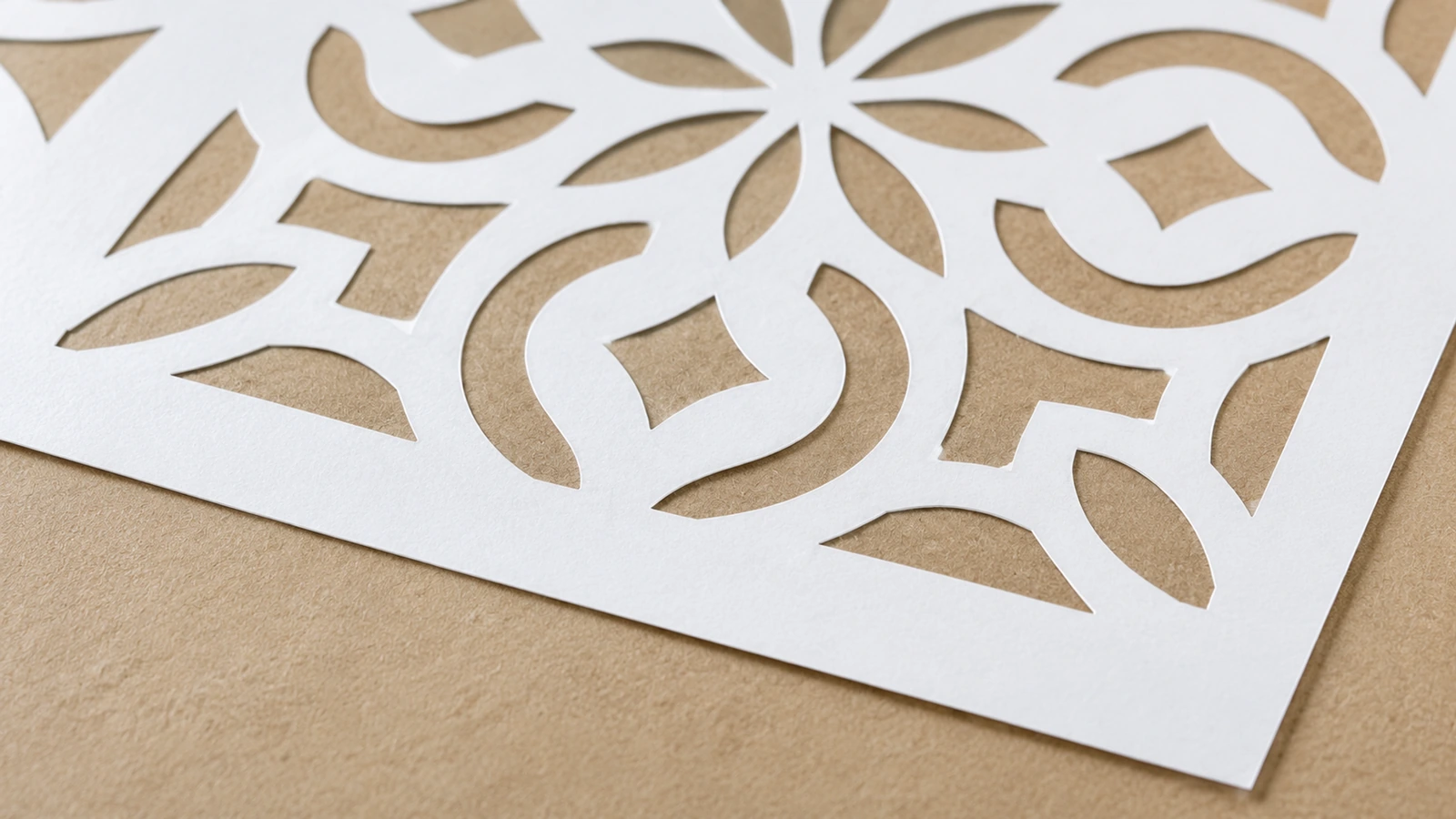Primo piano di intagli curvi e a forma di petalo in uno stencil bianco su una superficie beige